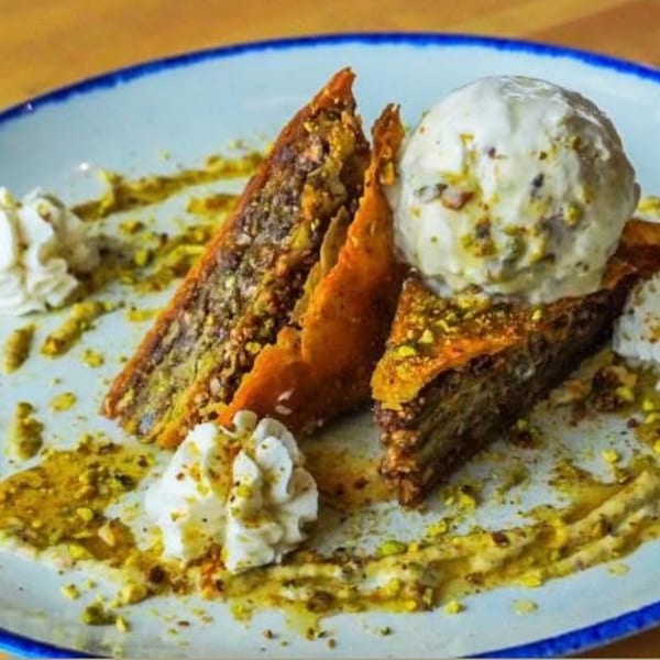 Two slices of baklava with a scoop of ice cream, whipped cream, and pistachio crumbles.