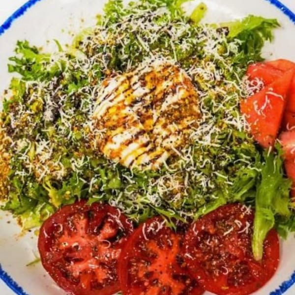 Mediterranean salad with greens, grilled halloumi cheese, sliced tomatoes, and watermelon on a white plate.
