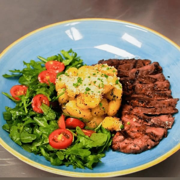 Grilled steak slices, roasted potatoes, and a fresh arugula salad with cherry tomatoes on a blue plate.