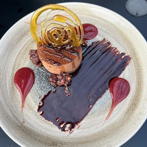 A chocolate mousse dessert with a caramel swirl, chocolate sauce, and raspberry coulis on a plate.