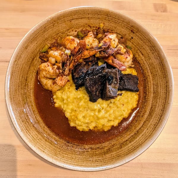 A Mediterranean dish with yellow risotto, dark meat, and seasoned shrimp in a brown sauce.