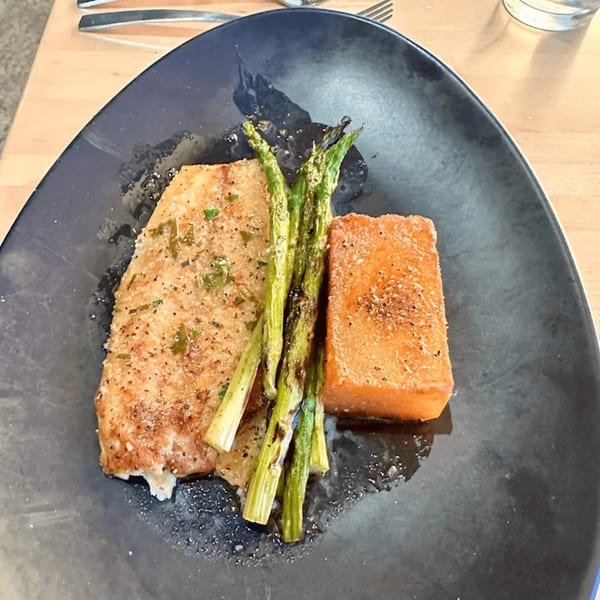 Mediterranean dish with a golden-brown fish fillet, grilled asparagus, and a rectangular sweet potato block.