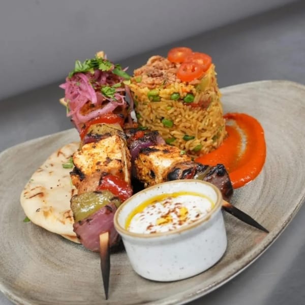 Mediterranean chicken skewers with rice, pickled onions, flatbread, and a white dipping sauce.
