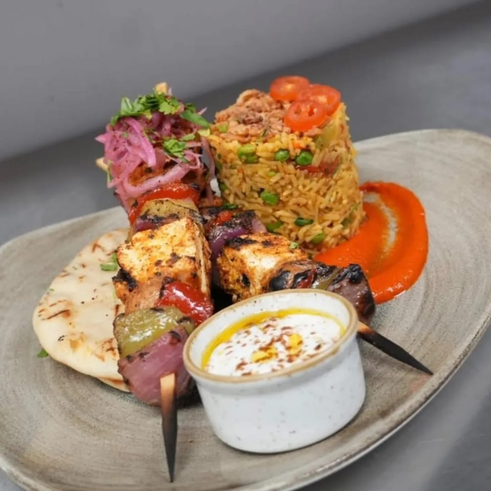 Mediterranean chicken skewers with rice, pickled onions, flatbread, and a white dipping sauce.